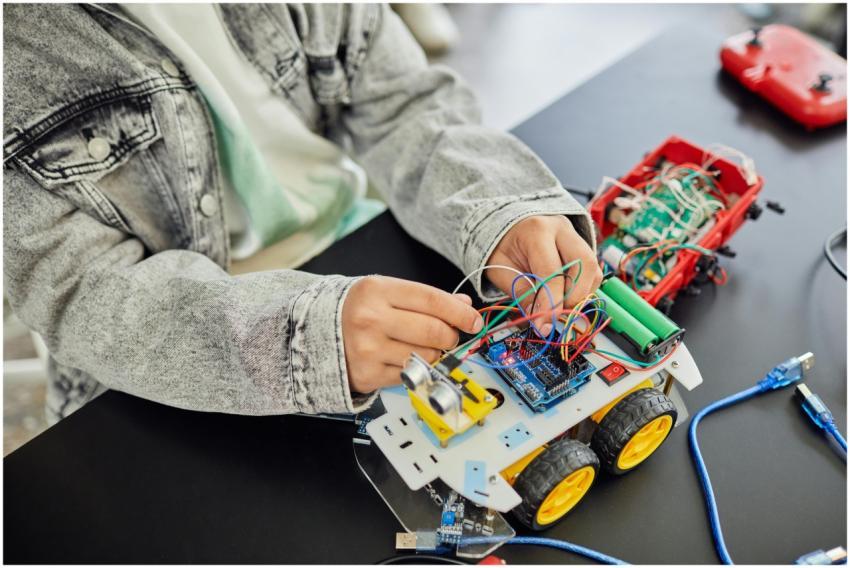 Young student assembling a toy car with electronic