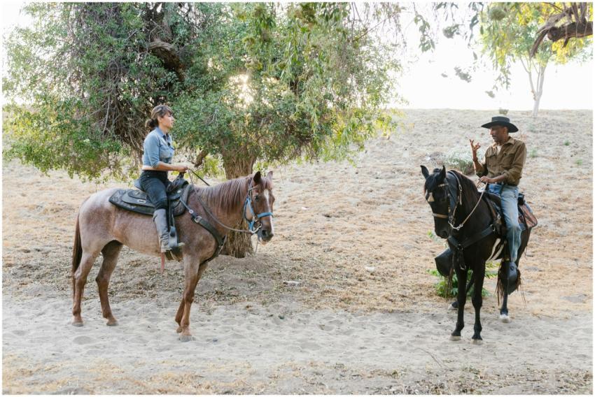 Two people riding horses on a sunny day at a ranch