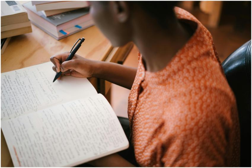 Focused black woman writing in a notebook with sta