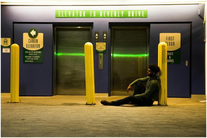 A man sitting by an elevator entrance under neon l