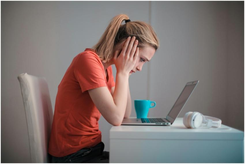 A woman sits indoors at a table, looking concerned