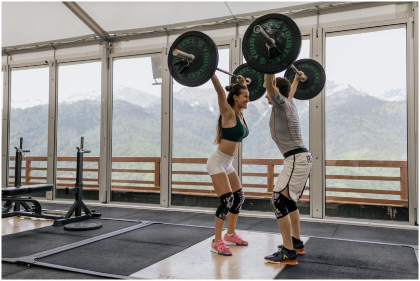 A couple lifting barbells together in a gym with s