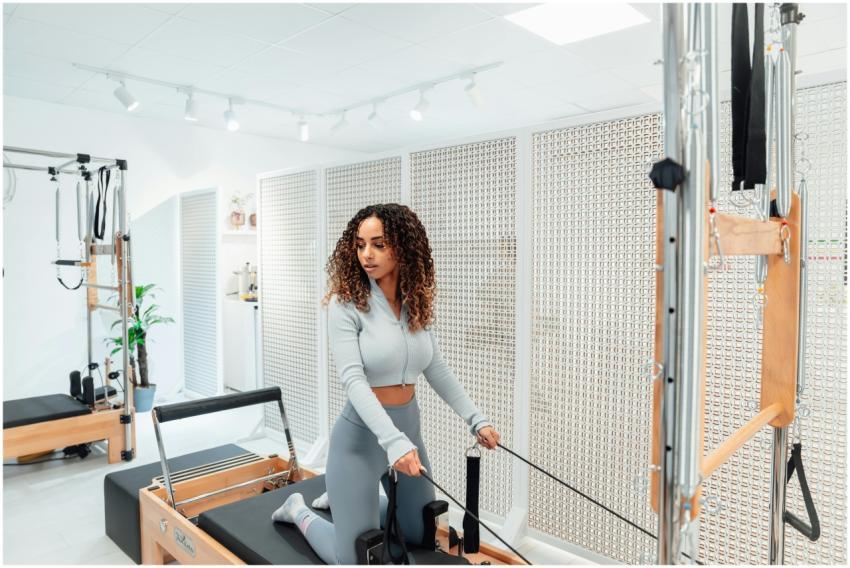 A woman in a gray tracksuit exercises on a Pilates