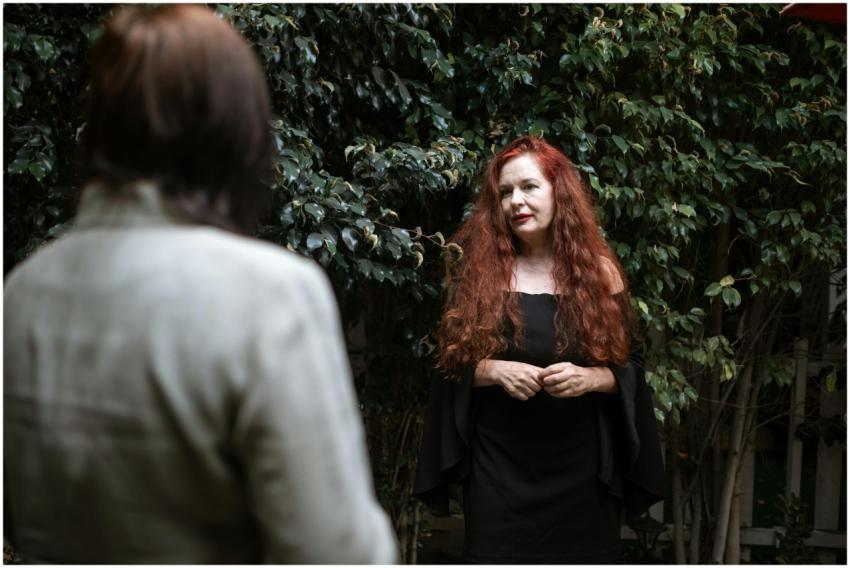 Red-haired woman in black dress among greenery, en