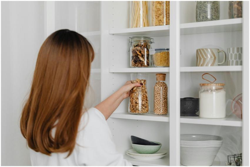 Woman arranging jars on pantry shelves for organiz