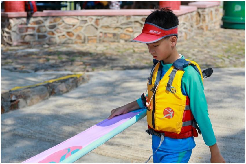 A child carries a colorful windsurf board wearing