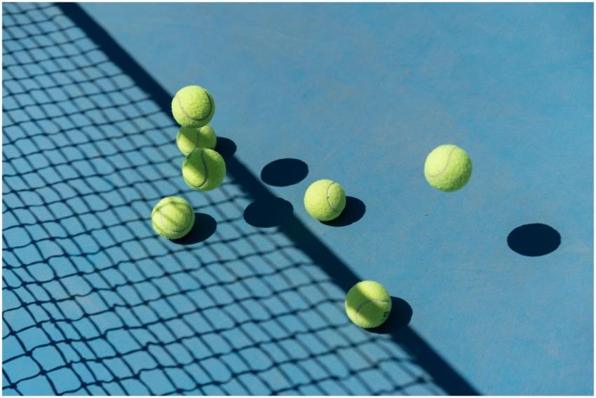 Tennis balls scattered on a blue court casting sha