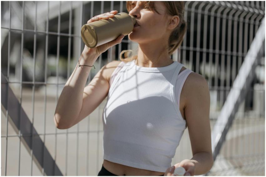 Woman in white tank top drinking from a tumbler ou