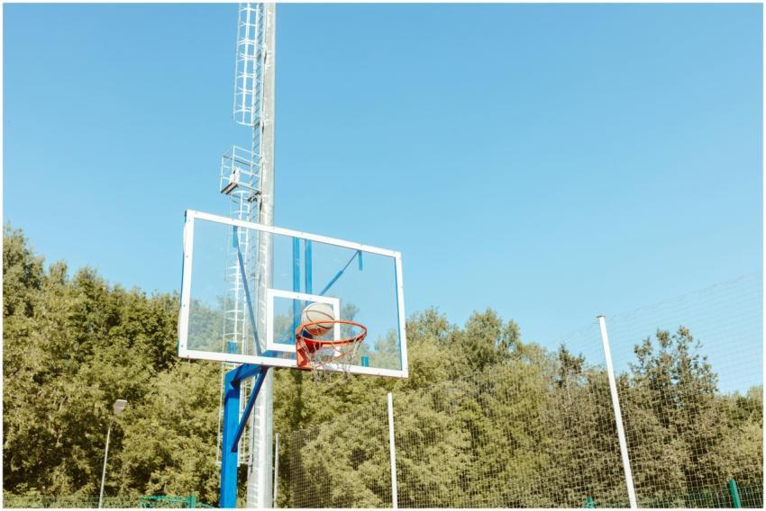 Basketball on hoop outdoors under a clear blue sky