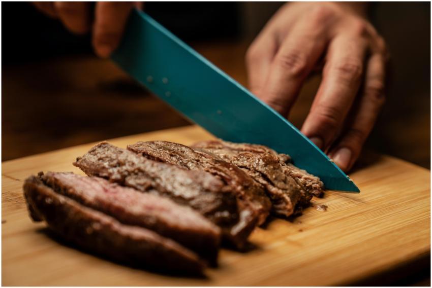 Hands slicing tender, juicy grilled steak on a woo