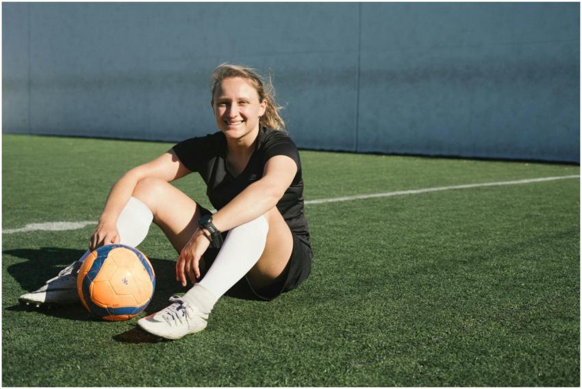 A smiling female soccer player sitting on a soccer