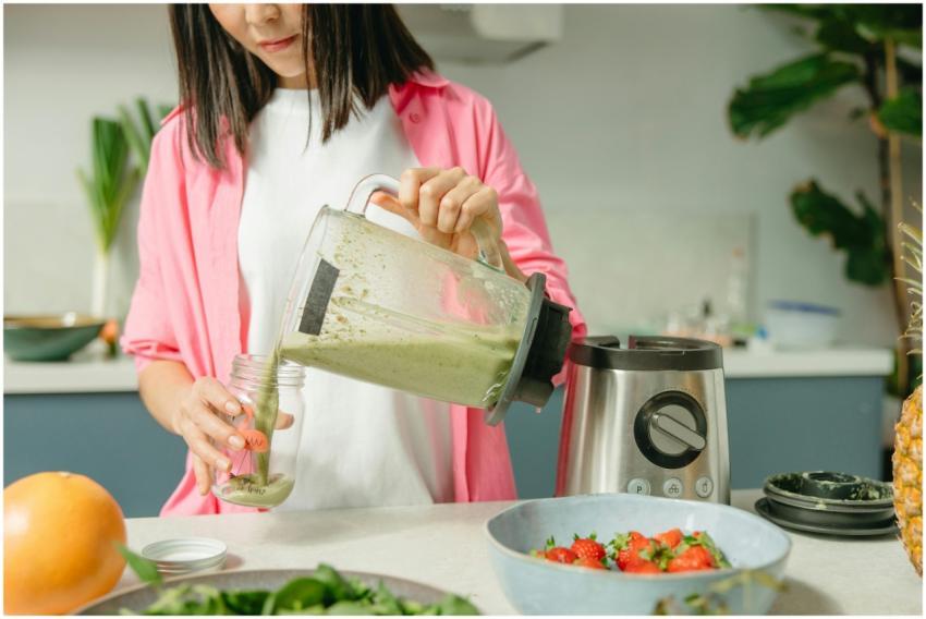 Woman making nutritious green smoothie in kitchen