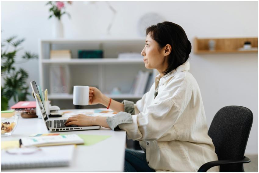Asian woman working on laptop while holding a coff