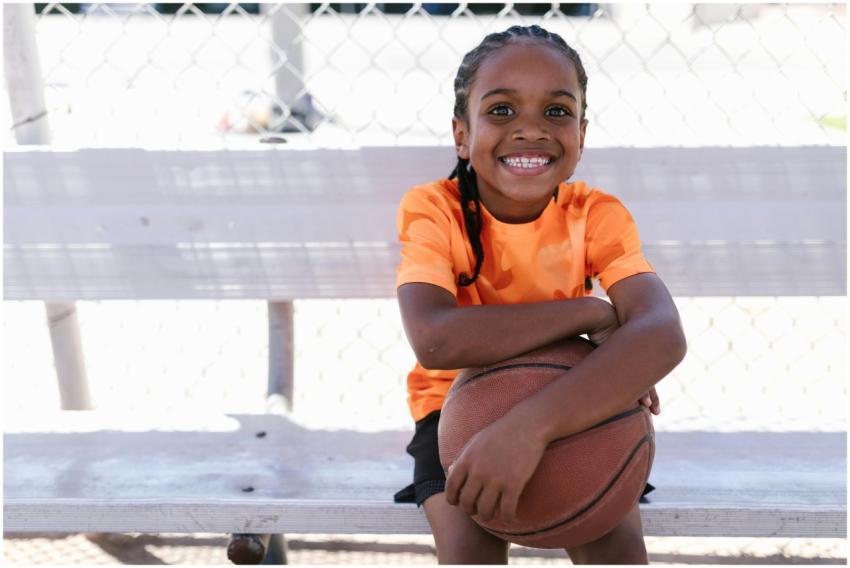 A young girl in an orange shirt, smiling, holding