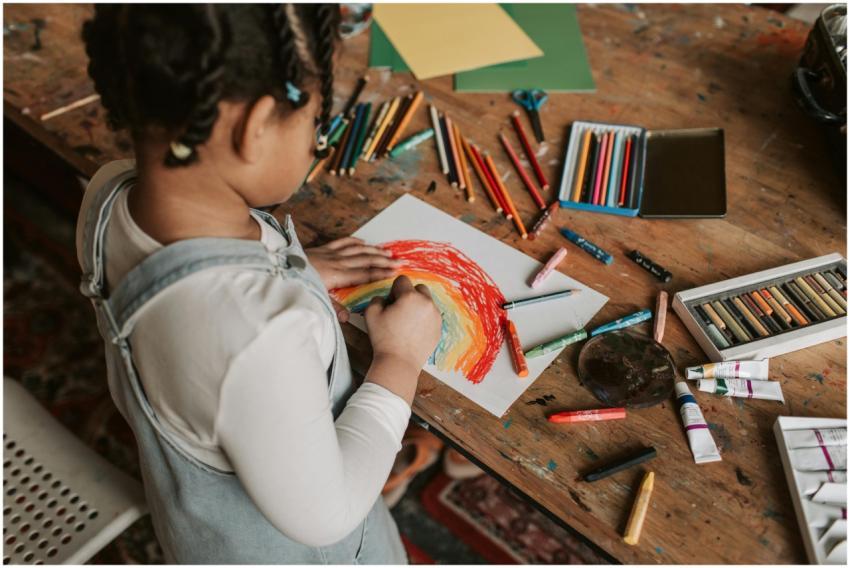 Young child creating a vibrant rainbow drawing at