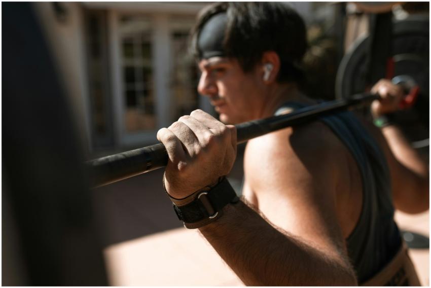 Man lifting barbell outdoors with focus on his gri