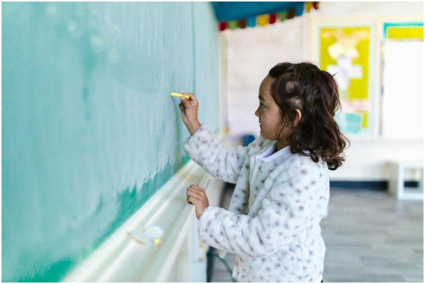 A young girl writing with chalk on a classroom bla