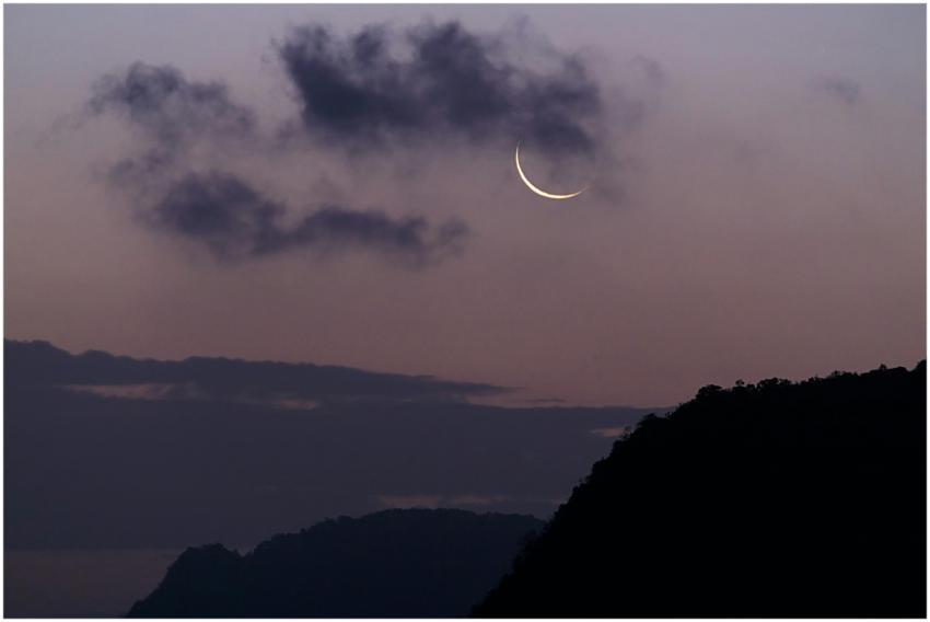 Crescent moon with dark clouds in twilight sky ove