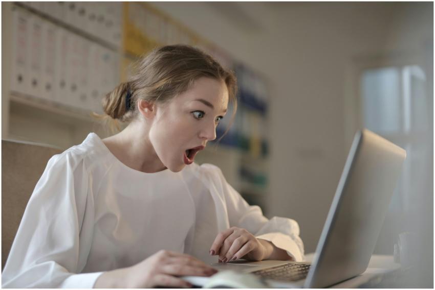 Surprised woman sitting at desk with laptop indoor