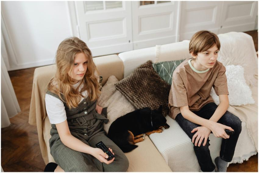 Two kids sitting on a couch with a pet dog indoors