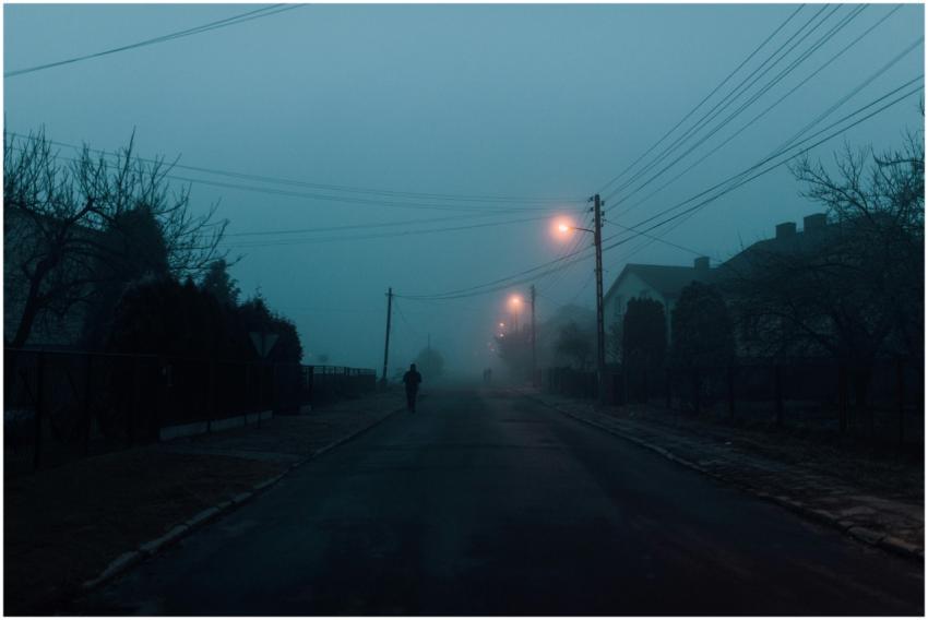 A lone person walks on a foggy street illuminated