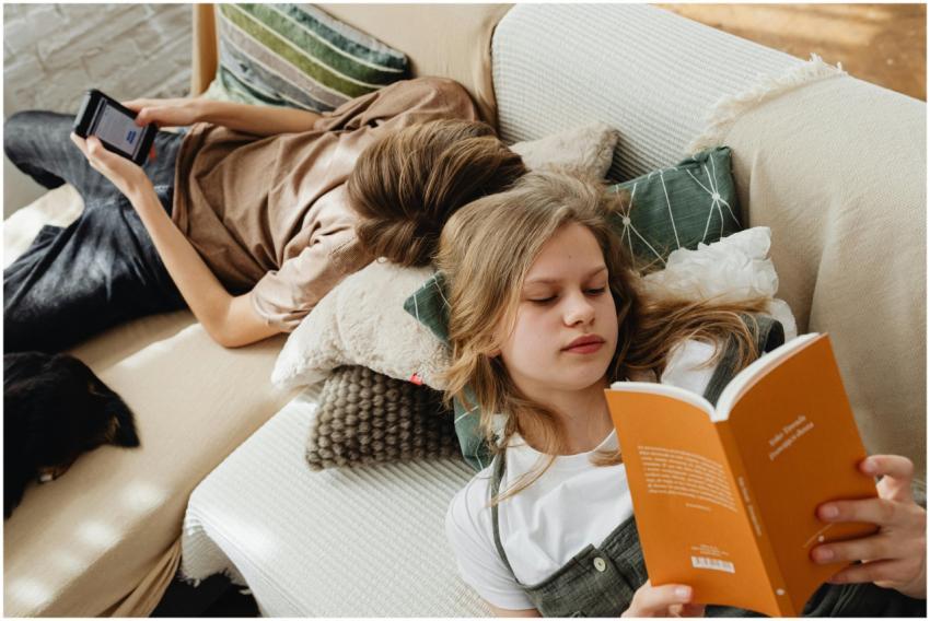 Two teenagers relaxing at home, reading and using