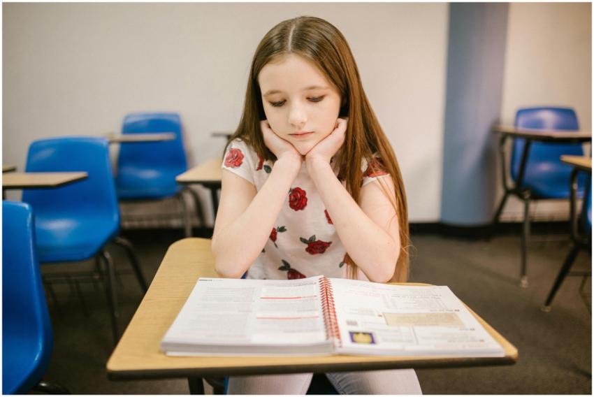 A young girl sits thoughtfully at her desk in a cl