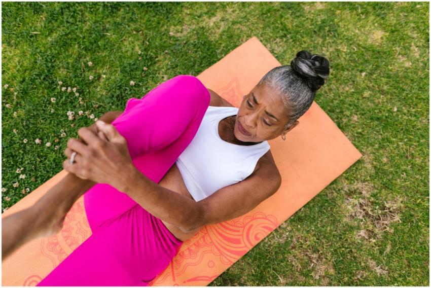 Elderly woman performing yoga stretch on grass for