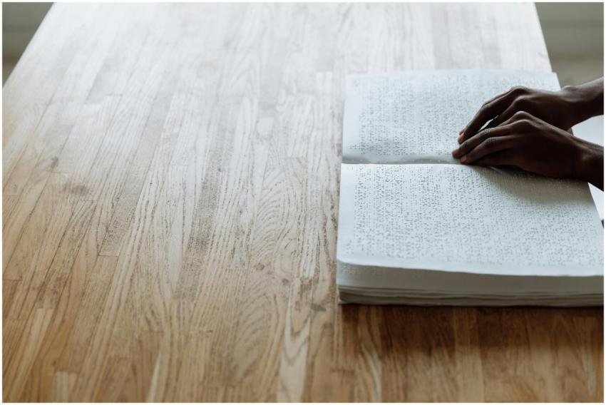 Person reading a Braille book on a wooden table, h