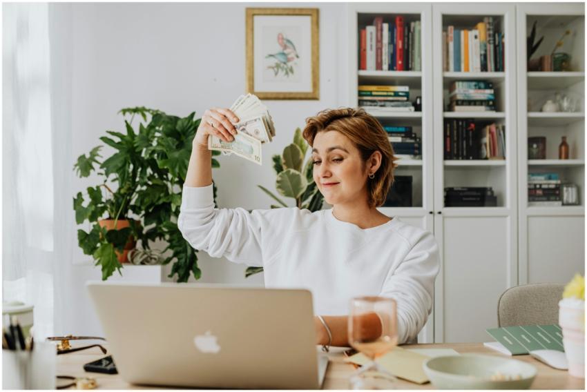 Smiling woman holding cash while working on a lapt