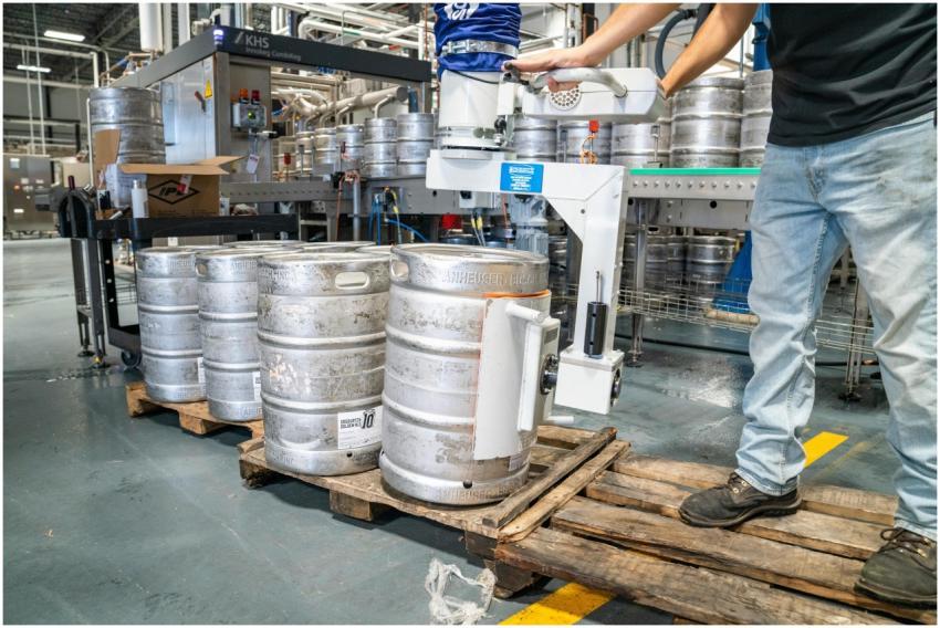 A worker operates machinery to stack steel kegs in