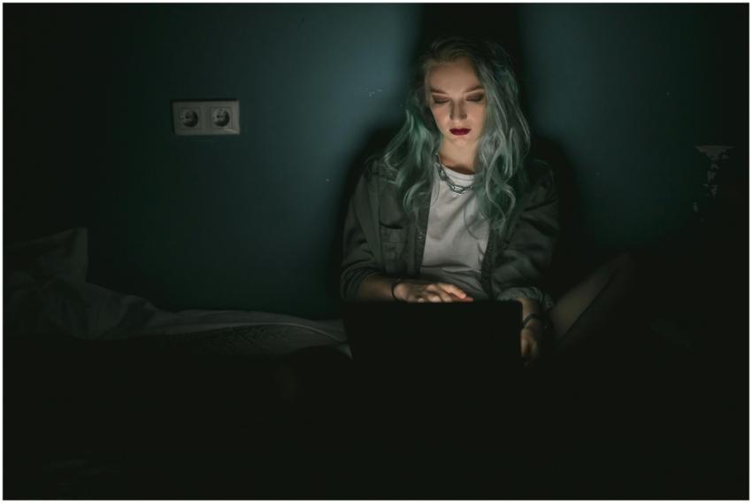 A woman with dyed hair using a laptop in a dimly l