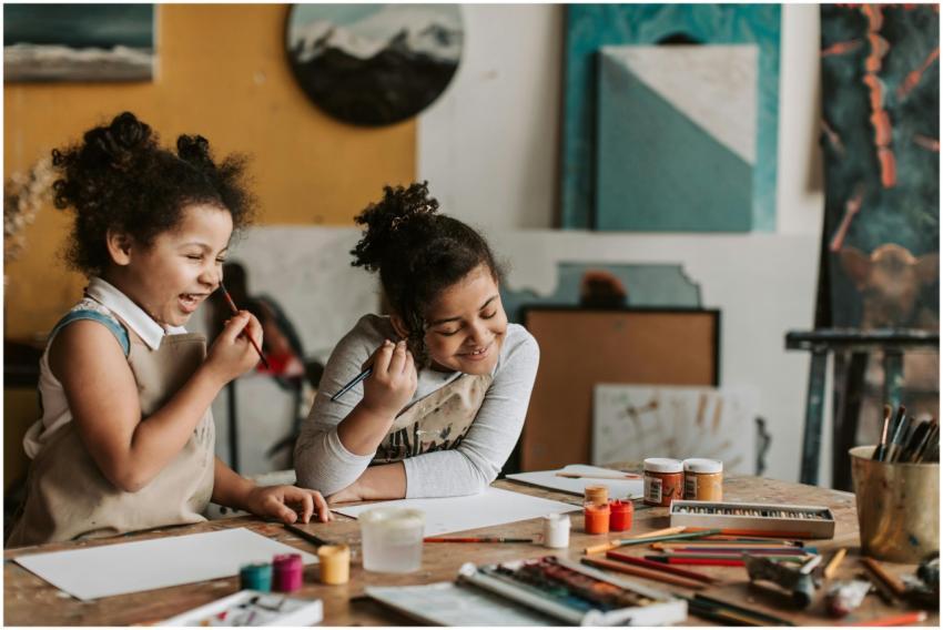 Two young girls happily painting during an indoor