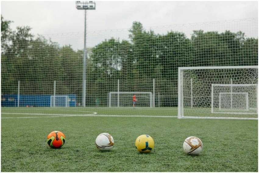 Four soccer balls on an outdoor field near goalpos