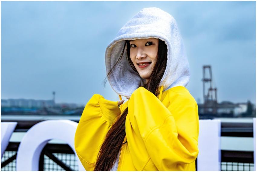 Smiling woman in yellow jacket with hood up, stand