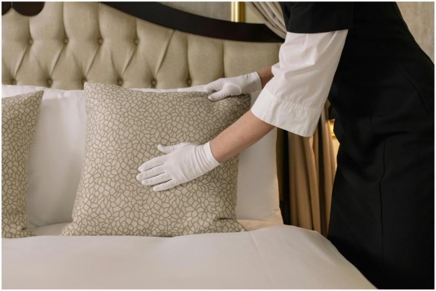 A housekeeper wearing gloves arranges pillows on a