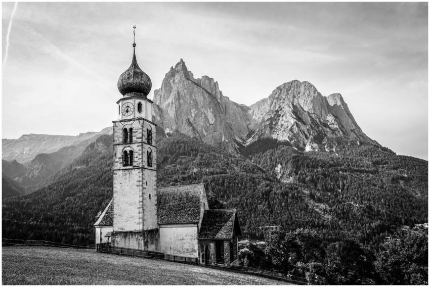 A black and white image of a church against a stun