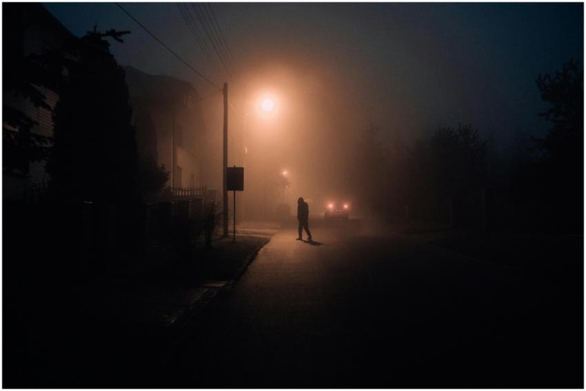 A lone silhouette walking down a foggy street at n