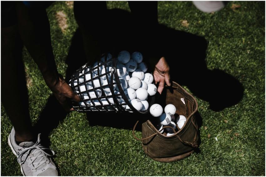 Person transferring golf balls into a bag on a gra