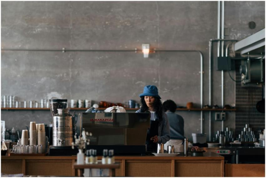 A barista wearing a blue hat operates a coffee mac