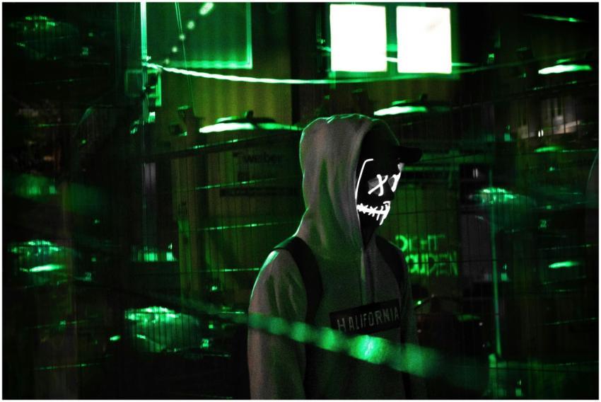 Man in a hoodie with glowing mask amidst neon gree