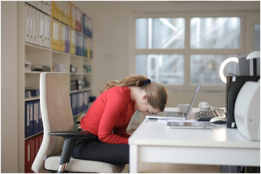 Tired woman in red sweater naps on office desk bes