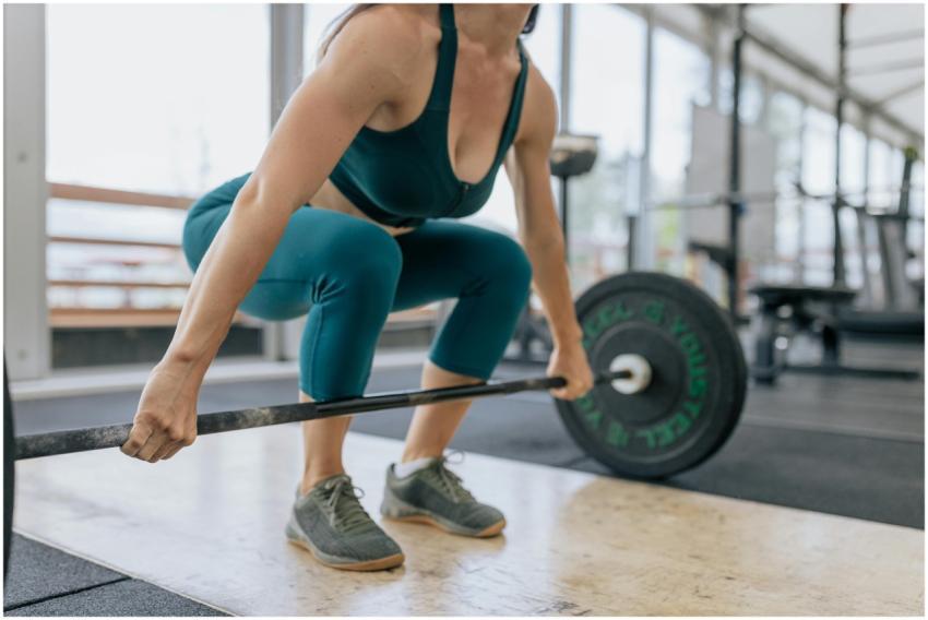 A woman in activewear lifting a barbell in a gym,