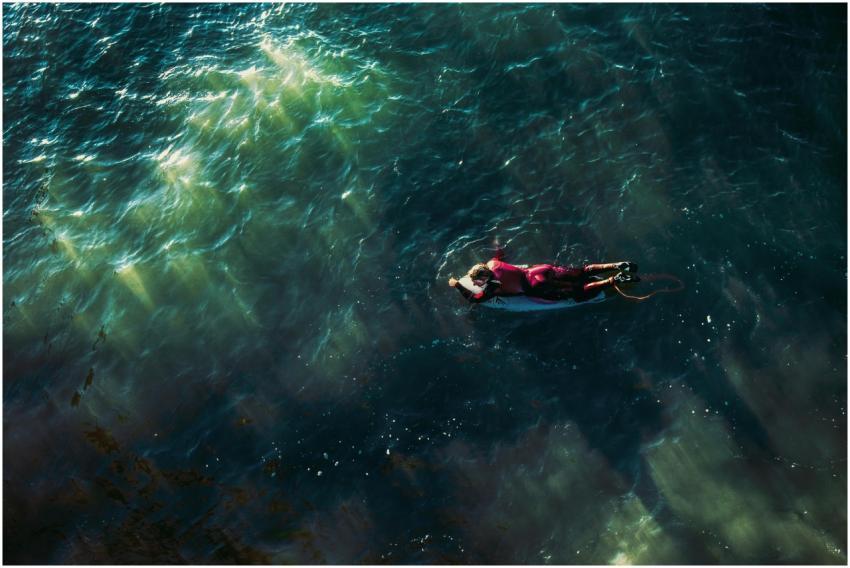 An aerial view of a lone surfer paddling in the de