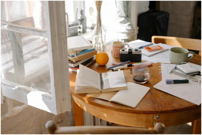 A cluttered study desk with open books, coffee, an