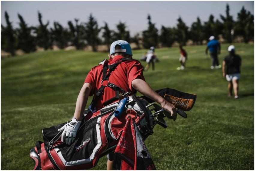 A golfer in red carrying a bag on a lush green gol