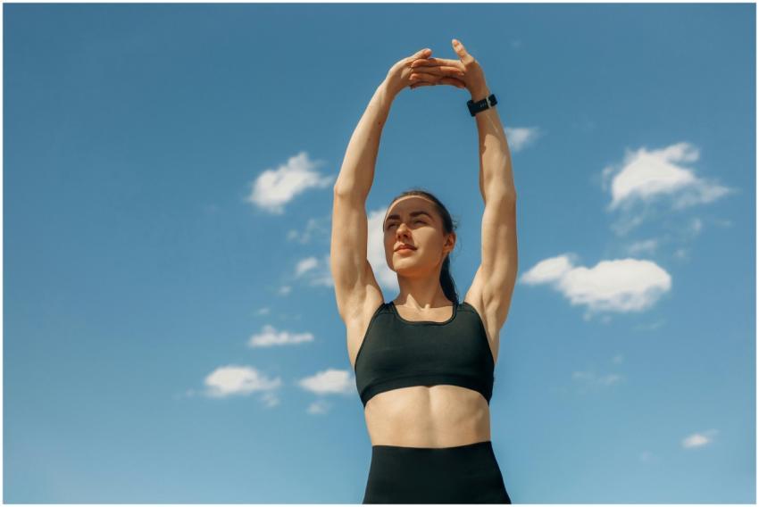Woman in sports bra stretching under a clear blue