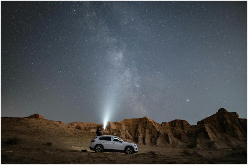 A person stands on an SUV under a vast starry nigh
