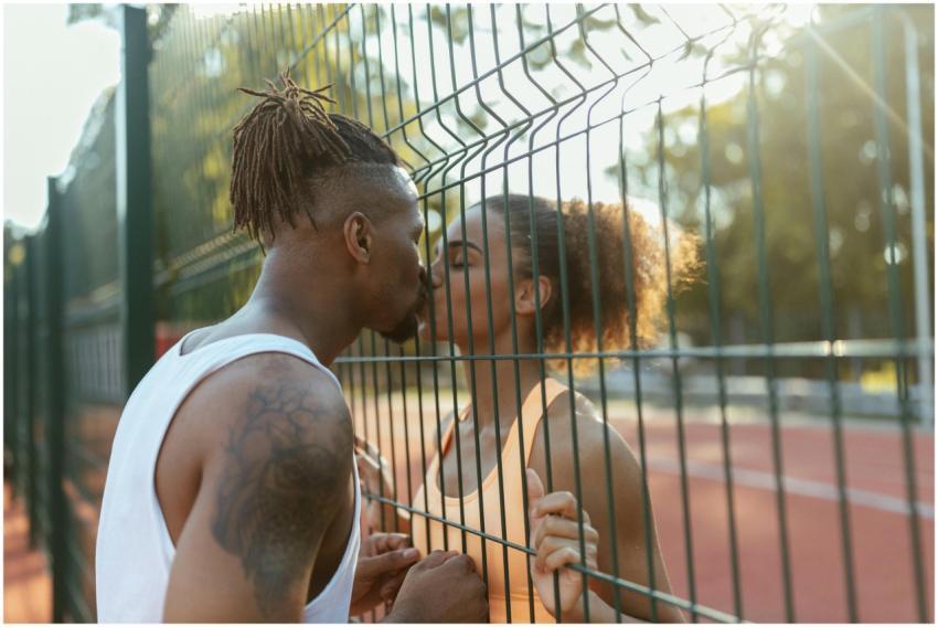 A couple shares a tender kiss through a fence on a