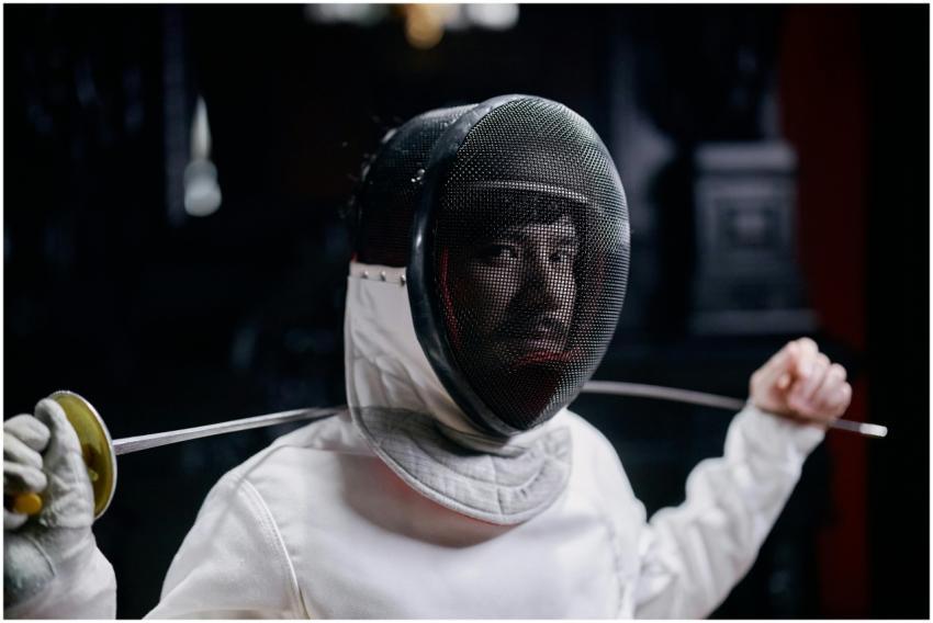 Fencer in full gear holding a foil, captured indoo